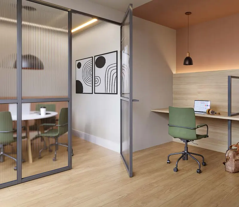 Espaço coworking do Dom Park Residencial com sala de reunião envidraçada e bancada de trabalho
